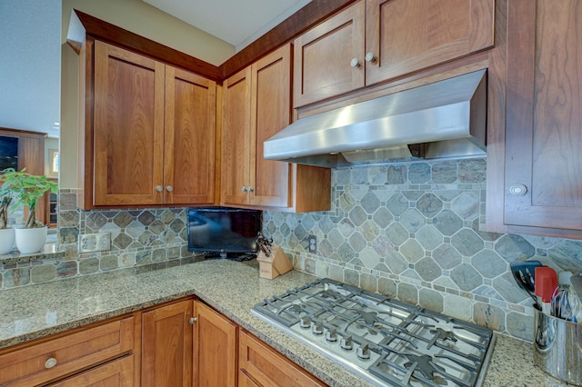 kitchen featuring stainless steel gas stovetop, ventilation hood, light stone countertops, and backsplash