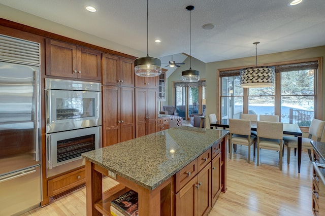 kitchen featuring multiple ovens, decorative light fixtures, stainless steel built in refrigerator, a center island, and light stone countertops