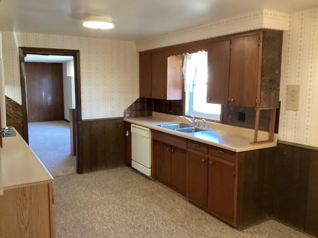 kitchen featuring wooden walls, white dishwasher, light colored carpet, and sink