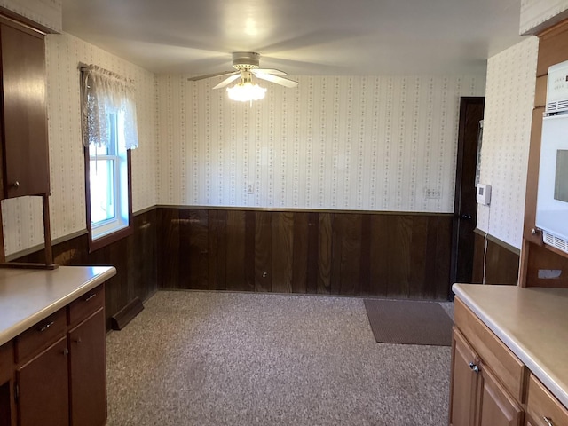 unfurnished dining area with wood walls, ceiling fan, and light carpet