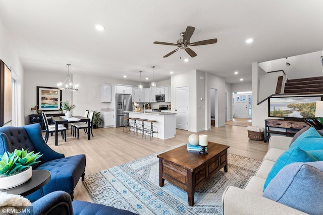 living room with ceiling fan with notable chandelier, light hardwood / wood-style floors, and sink