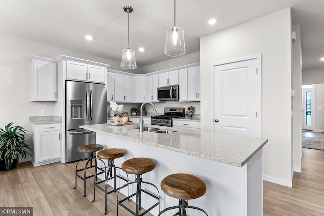 kitchen with light hardwood / wood-style flooring, white cabinets, a center island with sink, and appliances with stainless steel finishes