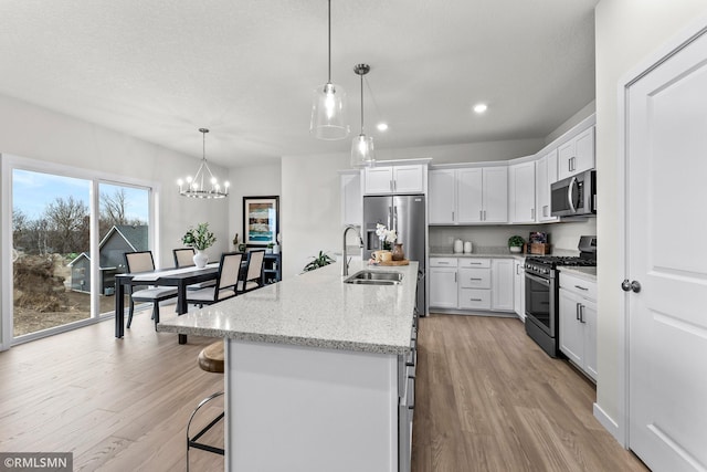 kitchen featuring hanging light fixtures, appliances with stainless steel finishes, a center island with sink, white cabinets, and light wood-type flooring