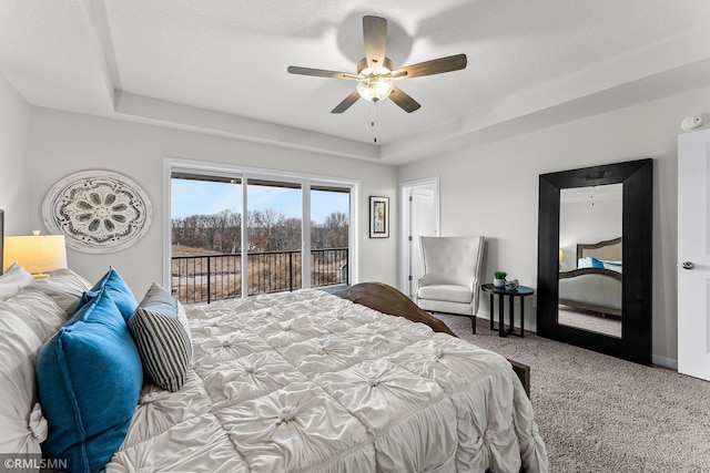 carpeted bedroom featuring ceiling fan, access to exterior, a textured ceiling, and a tray ceiling