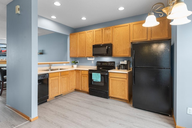 kitchen featuring decorative light fixtures, sink, light wood-type flooring, and black appliances