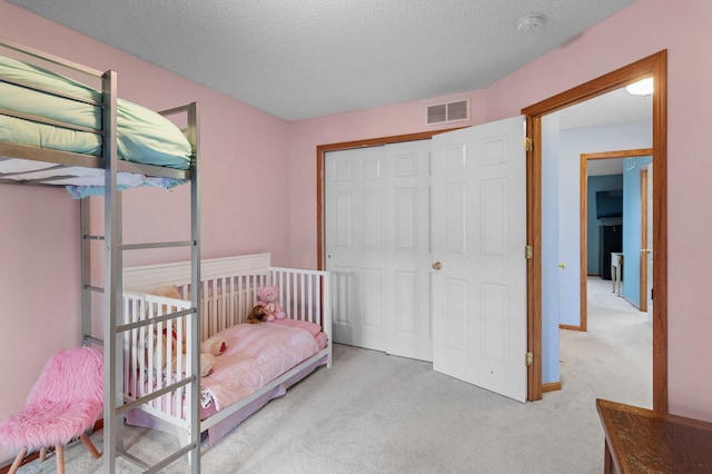 bedroom featuring light colored carpet, a textured ceiling, and a closet