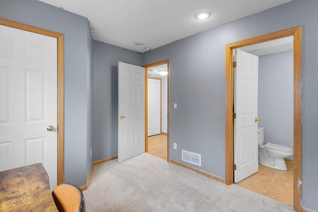 bedroom featuring light colored carpet, ensuite bath, and a textured ceiling