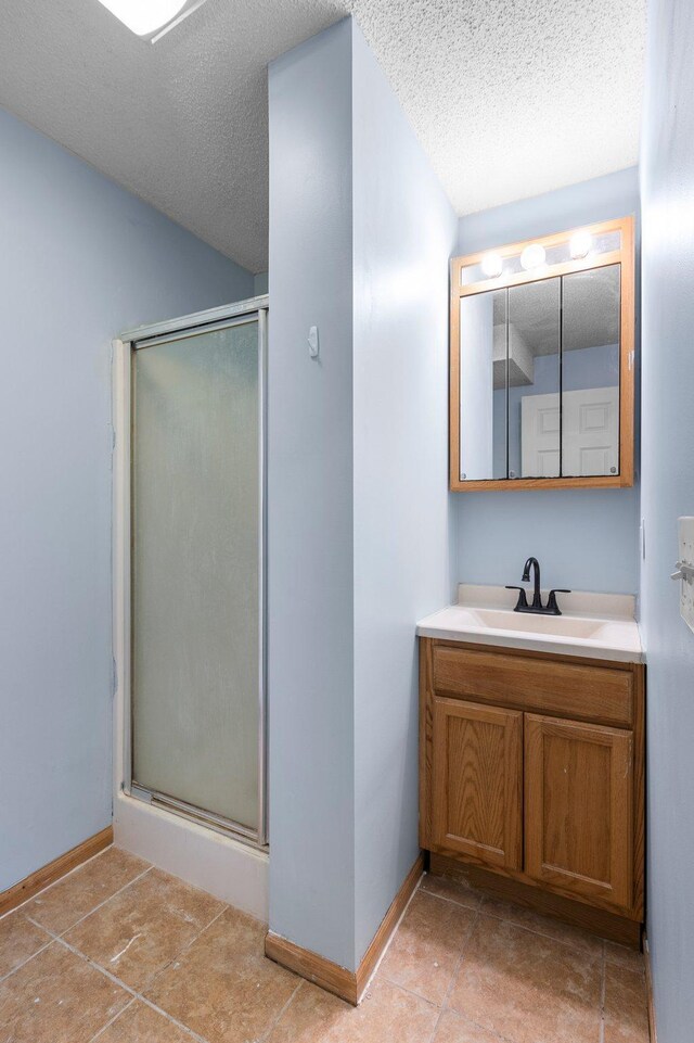 bathroom featuring an enclosed shower, vanity, tile patterned floors, and a textured ceiling