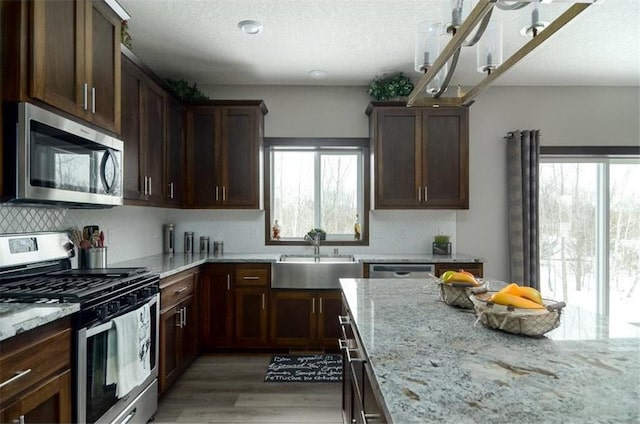 kitchen with sink, light hardwood / wood-style flooring, light stone countertops, appliances with stainless steel finishes, and dark brown cabinets