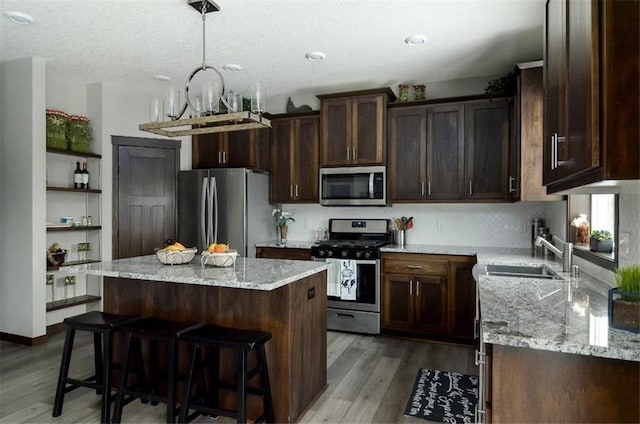 kitchen featuring light stone countertops, stainless steel appliances, sink, a center island, and light hardwood / wood-style floors