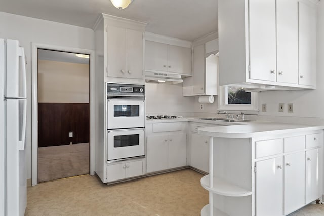 kitchen with sink, white appliances, kitchen peninsula, and white cabinets