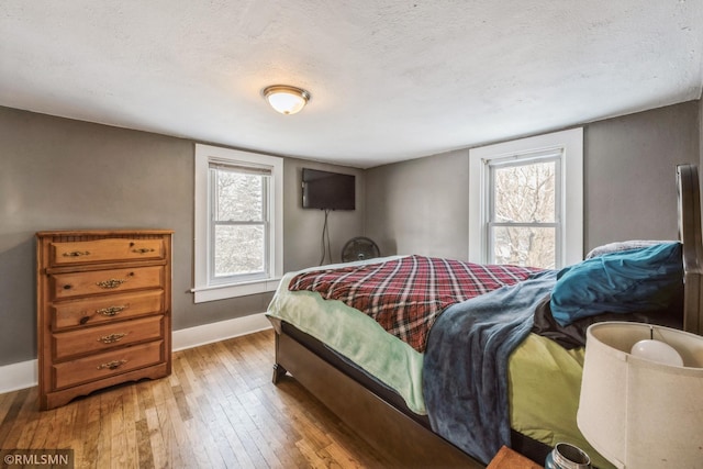 bedroom with a textured ceiling, light hardwood / wood-style flooring, and multiple windows