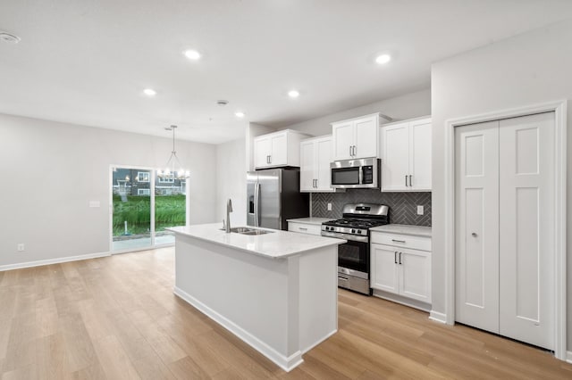 kitchen with an island with sink, pendant lighting, white cabinets, and stainless steel appliances