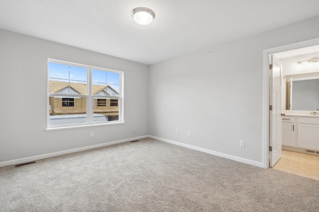 unfurnished bedroom featuring light colored carpet, ensuite bath, and sink