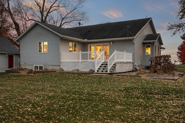 back house at dusk featuring a wooden deck and a lawn