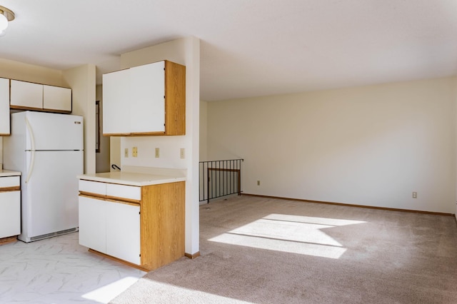 kitchen with white refrigerator, white cabinetry, and light carpet