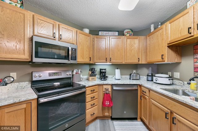 5650 Boone Ave N Unit 321, New Hope, MN 55428 - kitchen featuring appliances with stainless steel finishes, a textured ceiling, light wood finished floors, a sink, and light stone counters
