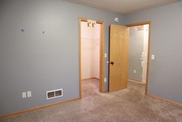 unfurnished bedroom featuring a textured ceiling, a spacious closet, carpet floors, and visible vents