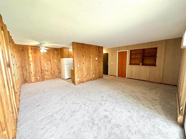 unfurnished living room with a textured ceiling, ceiling fan, wood walls, and light carpet