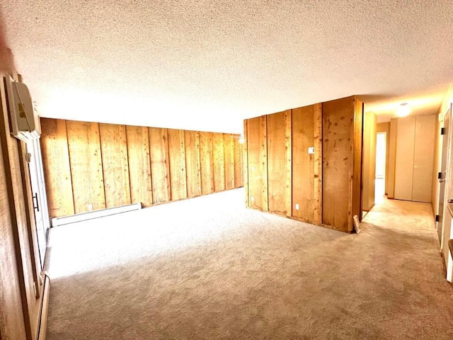 carpeted spare room with a textured ceiling, baseboard heating, and wood walls