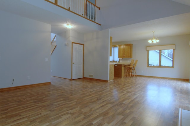 unfurnished living room with light wood-type flooring, a towering ceiling, and a chandelier