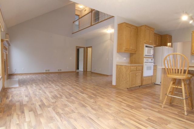 kitchen featuring white appliances, high vaulted ceiling, light hardwood / wood-style floors, and light brown cabinets