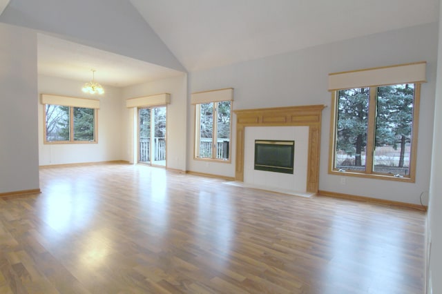 unfurnished living room featuring a tile fireplace, high vaulted ceiling, light hardwood / wood-style flooring, and a chandelier