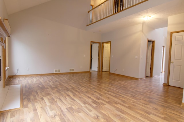 unfurnished living room featuring a towering ceiling, light wood-type flooring, and a tiled fireplace