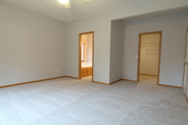 unfurnished bedroom with a spacious closet, connected bathroom, ceiling fan, a closet, and light colored carpet