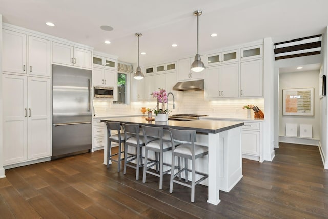 kitchen with white cabinets, built in appliances, dark hardwood / wood-style floors, and a kitchen island with sink