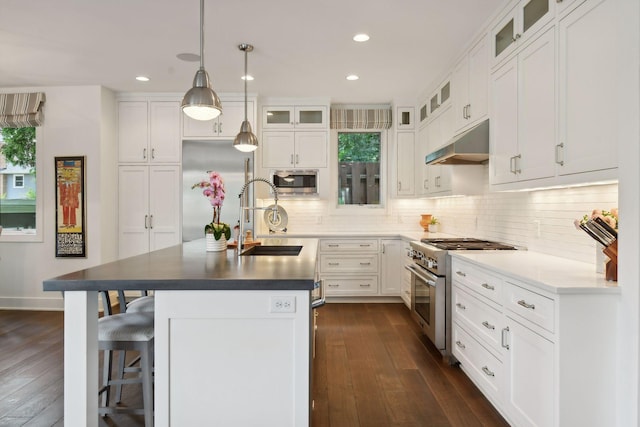 kitchen with built in appliances, dark hardwood / wood-style floors, white cabinetry, and an island with sink