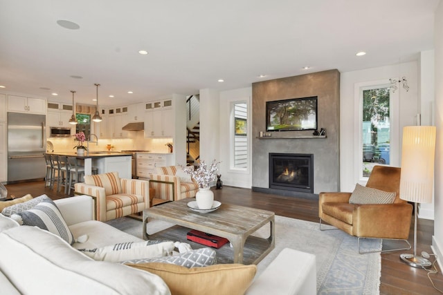 living room featuring a large fireplace, dark wood-type flooring, sink, and a healthy amount of sunlight