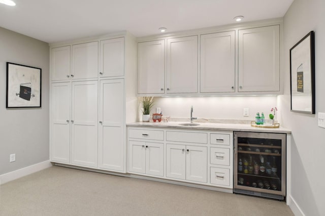 bar with light colored carpet, white cabinetry, beverage cooler, and sink