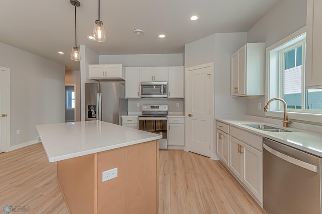 kitchen with appliances with stainless steel finishes, sink, light hardwood / wood-style flooring, a center island, and white cabinetry