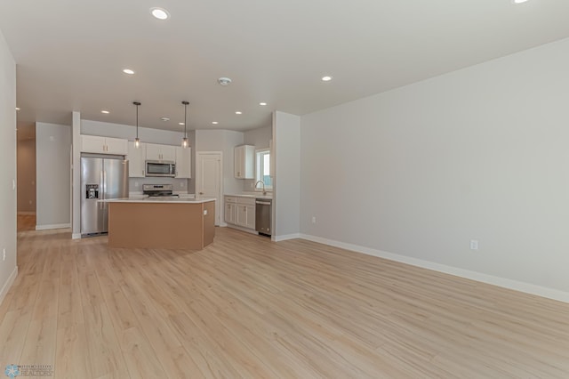 kitchen featuring light hardwood / wood-style flooring, decorative light fixtures, a kitchen island, white cabinetry, and stainless steel appliances