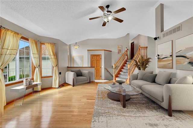 living room featuring a textured ceiling, light wood-type flooring, vaulted ceiling, and ceiling fan