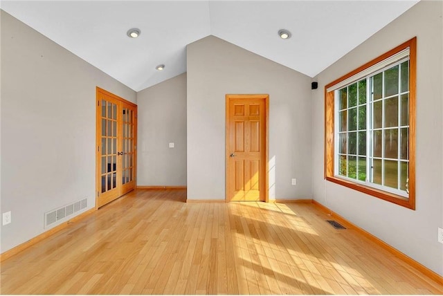 empty room with lofted ceiling, light wood-type flooring, french doors, and a healthy amount of sunlight