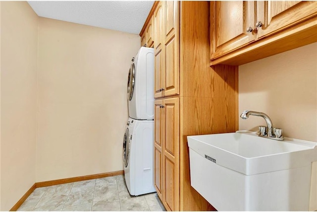 clothes washing area featuring cabinets, sink, stacked washing maching and dryer, and a textured ceiling