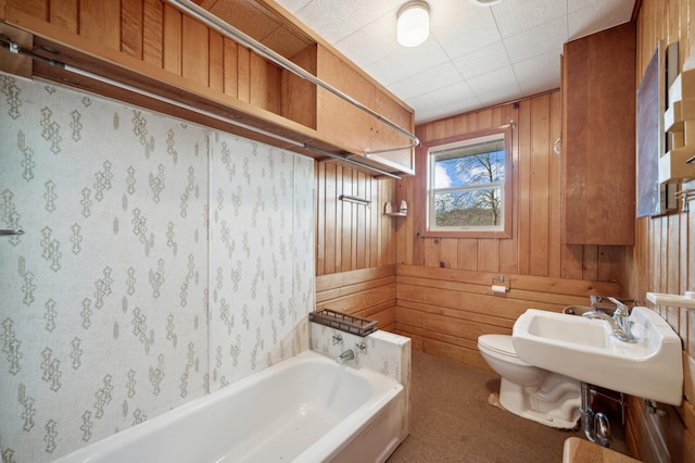 bathroom with a bathtub, toilet, sink, and wooden walls