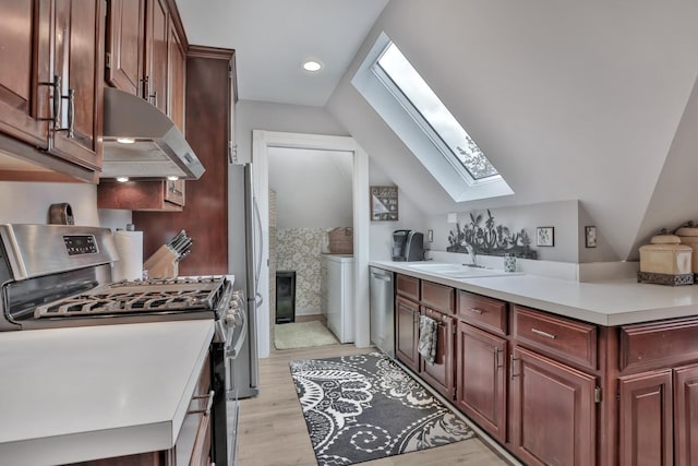 kitchen with vaulted ceiling with skylight, stainless steel appliances, sink, a fireplace, and light hardwood / wood-style floors