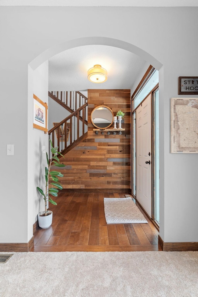 carpeted foyer with visible vents, arched walkways, wood walls, and baseboards