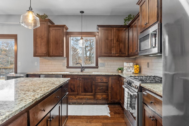 kitchen with light stone countertops, dark wood-style flooring, a sink, stainless steel appliances, and backsplash