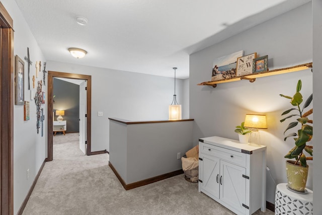 hall with an upstairs landing, light carpet, and baseboards