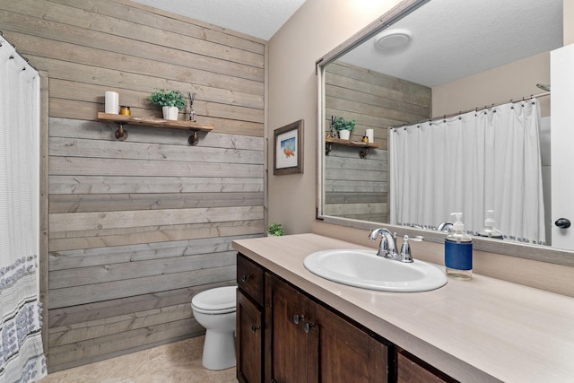 bathroom with vanity, toilet, wood walls, and a textured ceiling