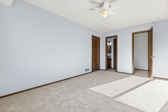 unfurnished bedroom with ceiling fan, connected bathroom, light carpet, and a textured ceiling