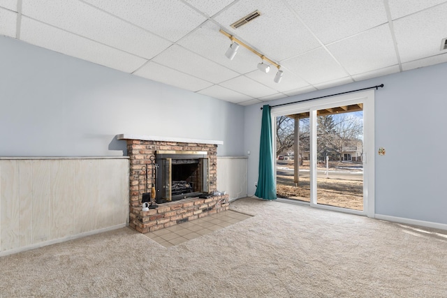 unfurnished living room featuring wood walls, rail lighting, carpet floors, a brick fireplace, and a drop ceiling