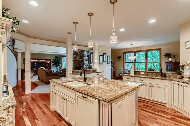 kitchen with light stone countertops, ornate columns, sink, light hardwood / wood-style floors, and hanging light fixtures