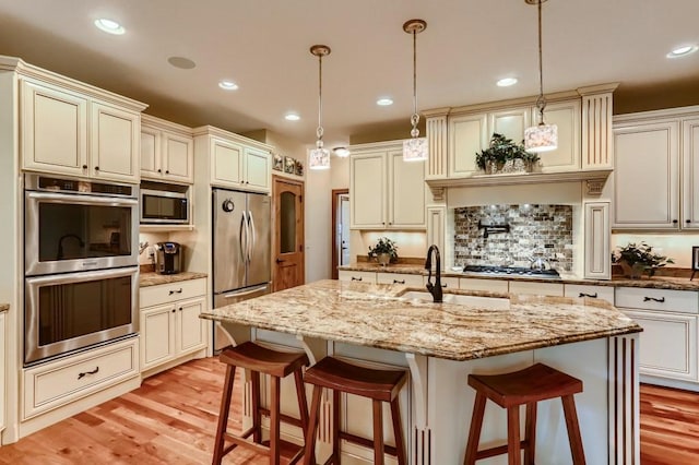 kitchen featuring stainless steel appliances, hanging light fixtures, a breakfast bar area, and an island with sink