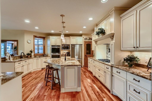 kitchen with hanging light fixtures, light hardwood / wood-style floors, a breakfast bar area, a center island with sink, and appliances with stainless steel finishes