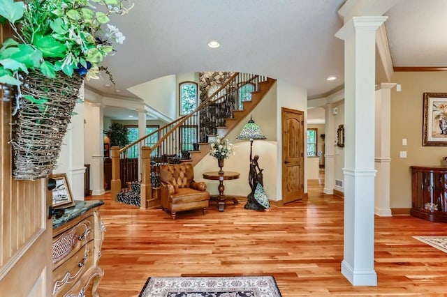 foyer featuring light wood-type flooring, ornate columns, and crown molding